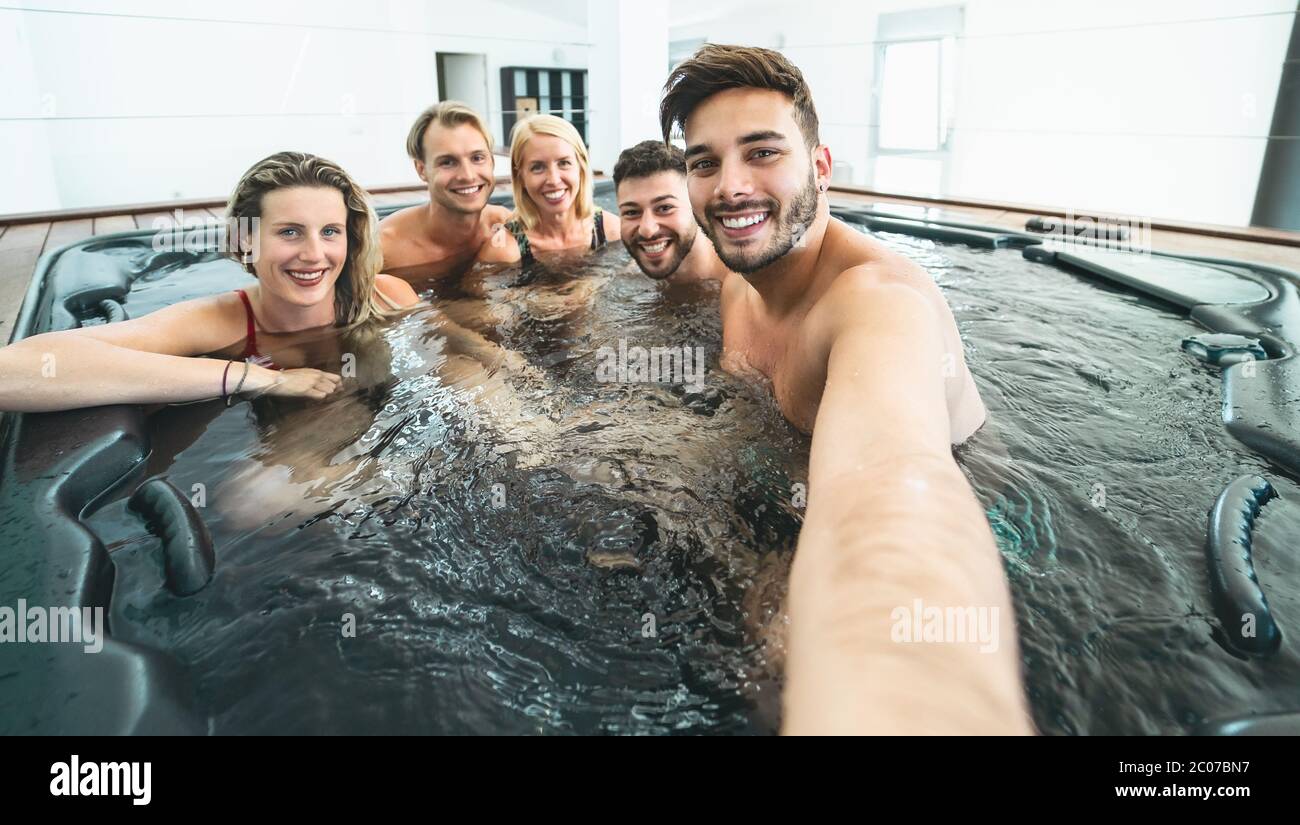Happy friends taking selfie while doing jacuzzi in luxury house - Young people having fun together in hot tub Stock Photo
