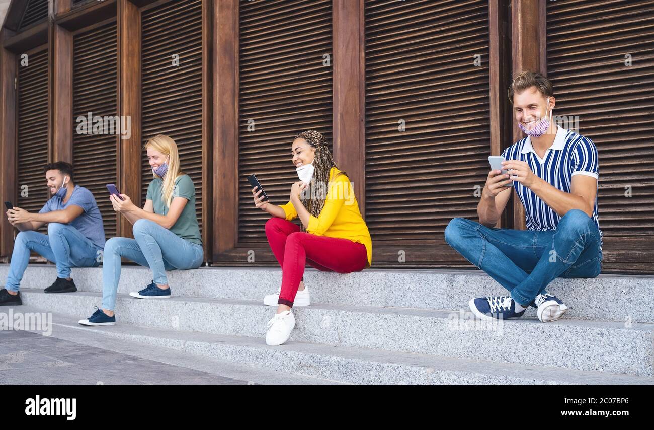 Young people using mobile phones while keeping social distance outdoor - Multiracial friends having fun watching on smartphones social networks apps Stock Photo