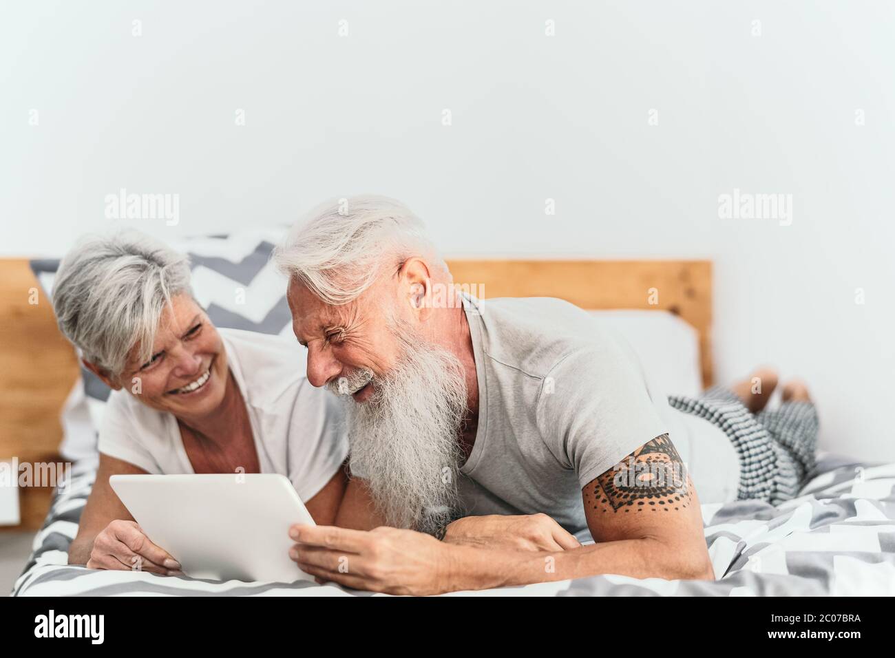 Happy senior couple using digital tablet in bed - Mature people having funny bed time together Stock Photo