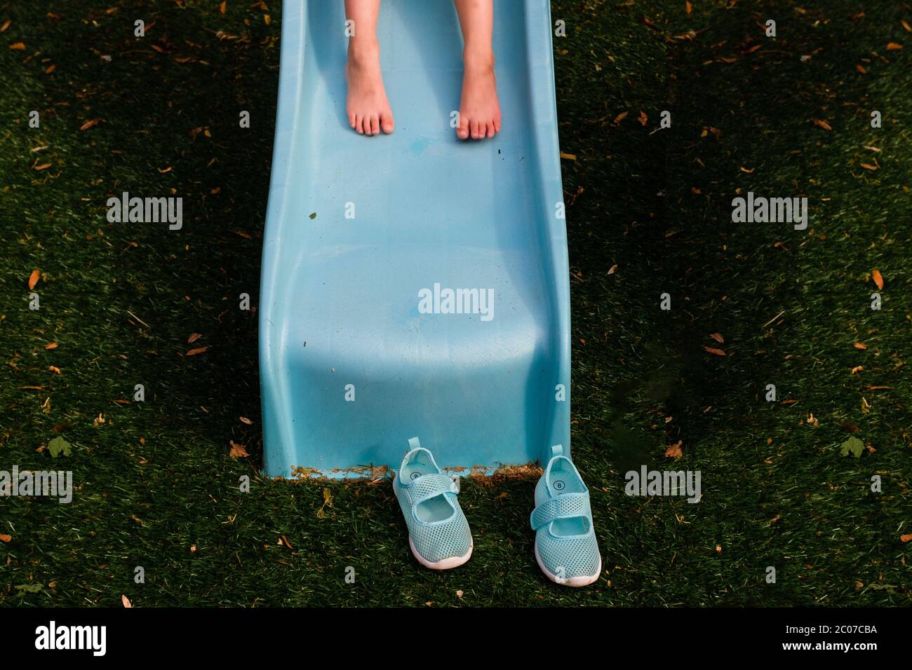 Barefoot child on blue slide with shoes on ground Stock Photo