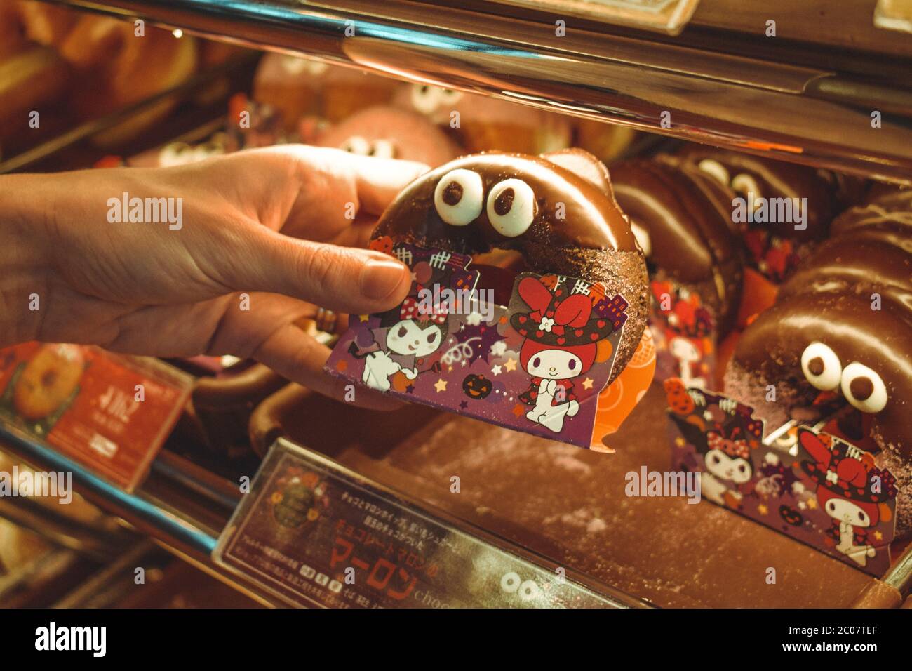 Female hand holding a cute Japanese chocolate doughnut with eyes Stock Photo