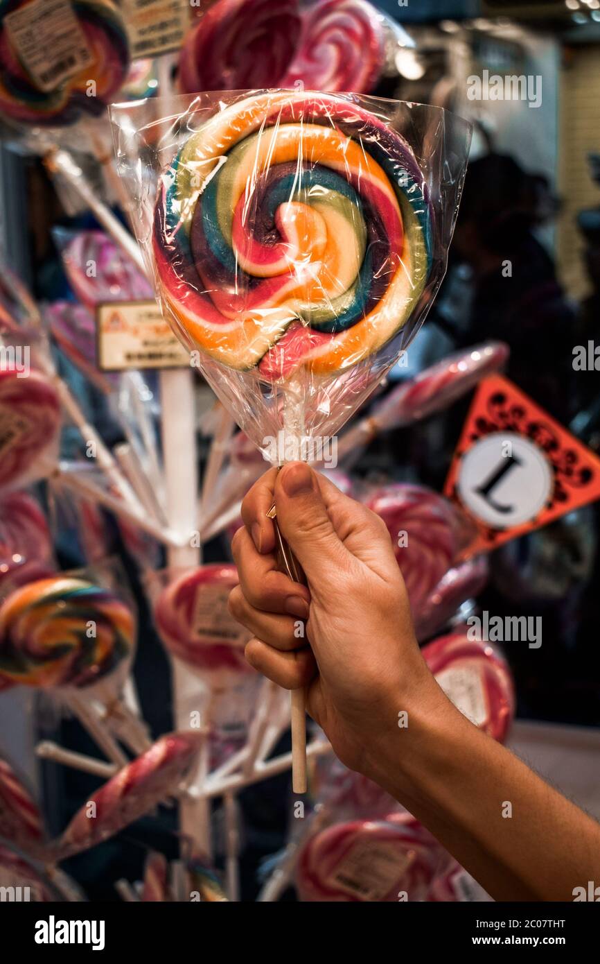 Female hand holding a rainbow colour colored lollipop in front of a holder with lollipops Stock Photo
