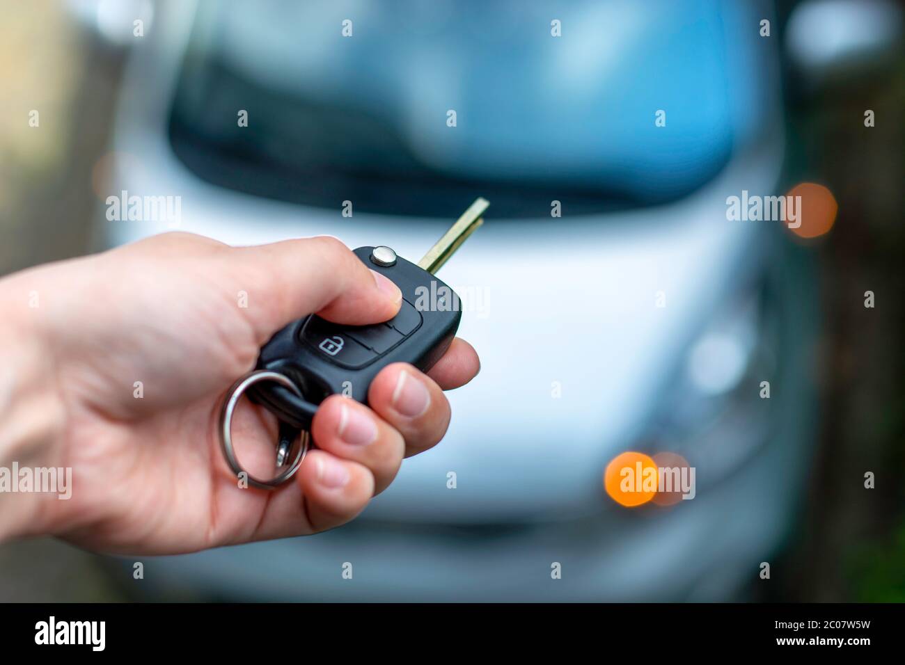 Women hand hand holding contactless car key and pressing the button on the remote to lock or unlock the car. Flashing lights of the car Stock Photo