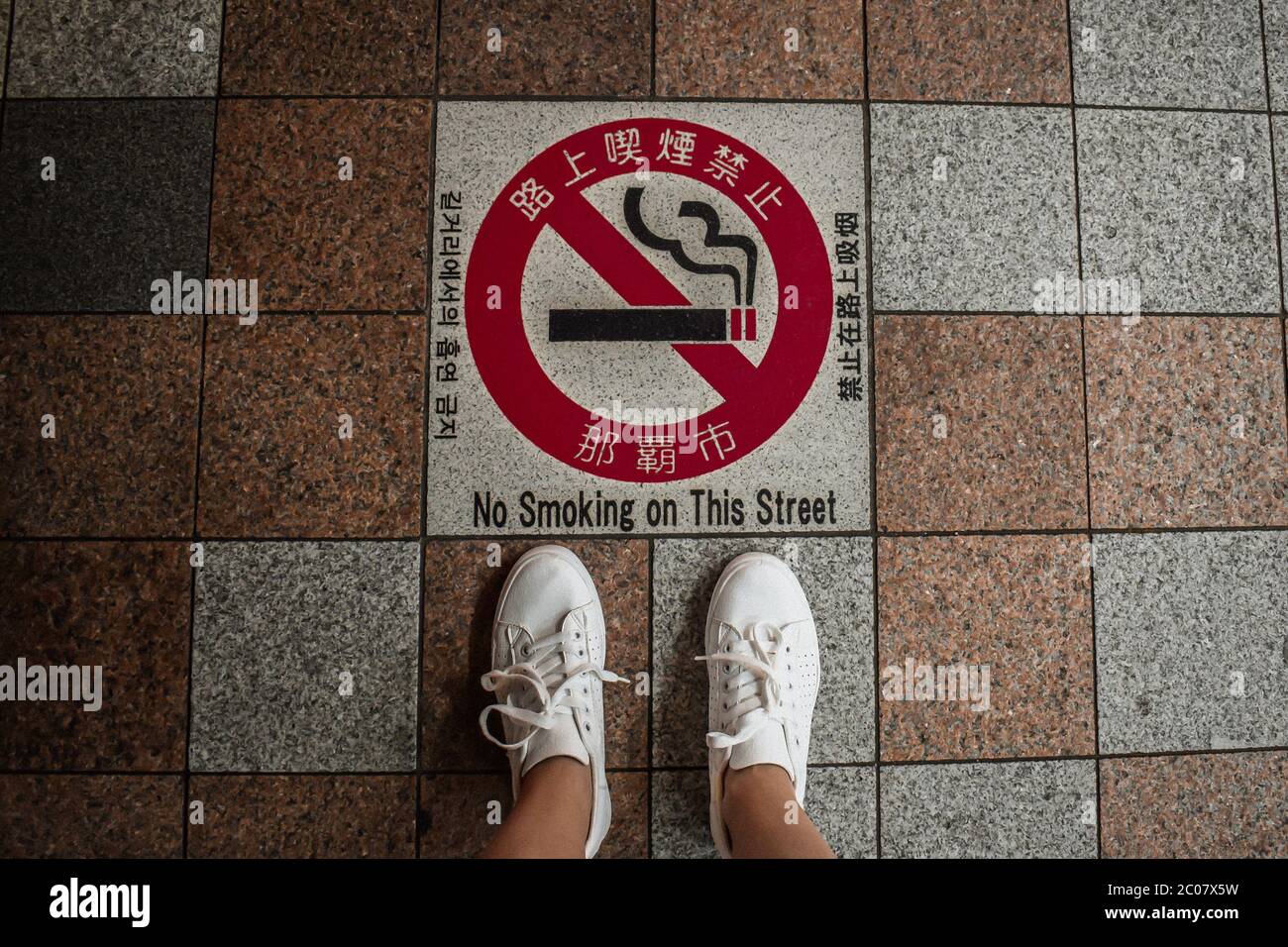 Legs in sneakers standing above a smoking prohibited sign written in Japanese in Tokyo Japan Stock Photo