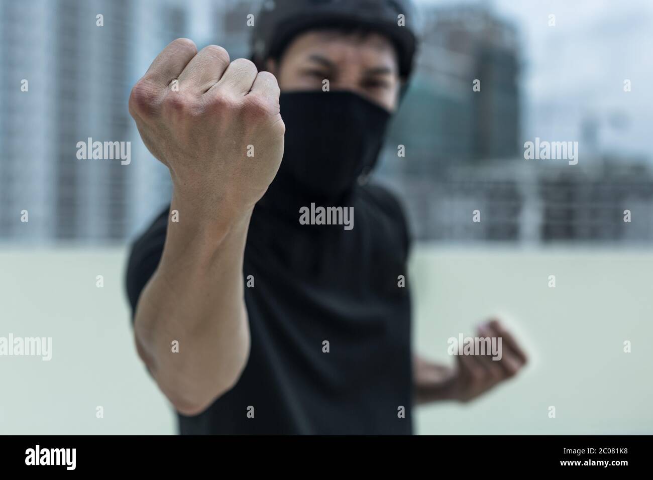 A protestor covered in a mask angry with his fist out standing in the city Stock Photo