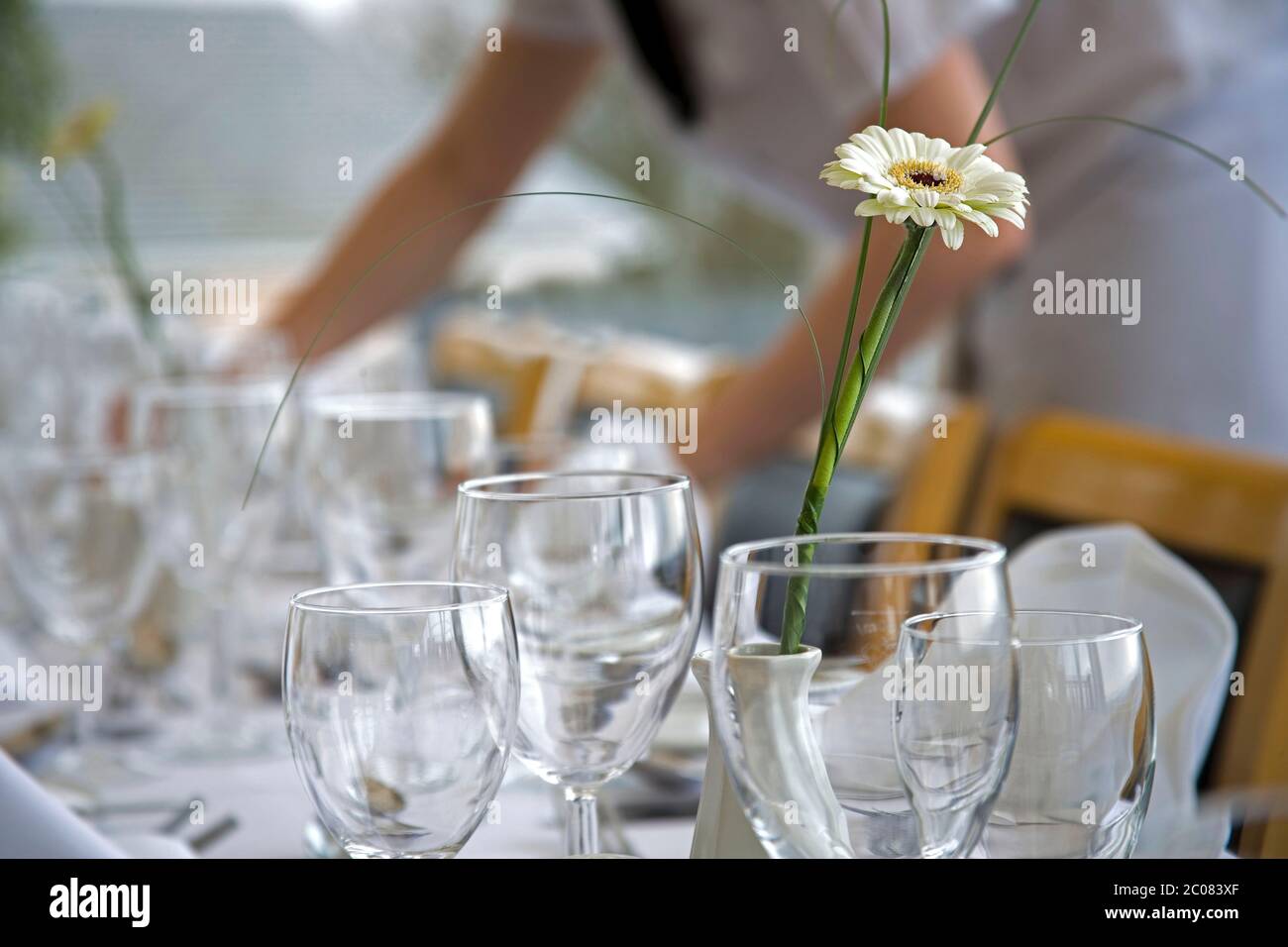 Dinner table being laid with wine glasses and flower display Stock Photo