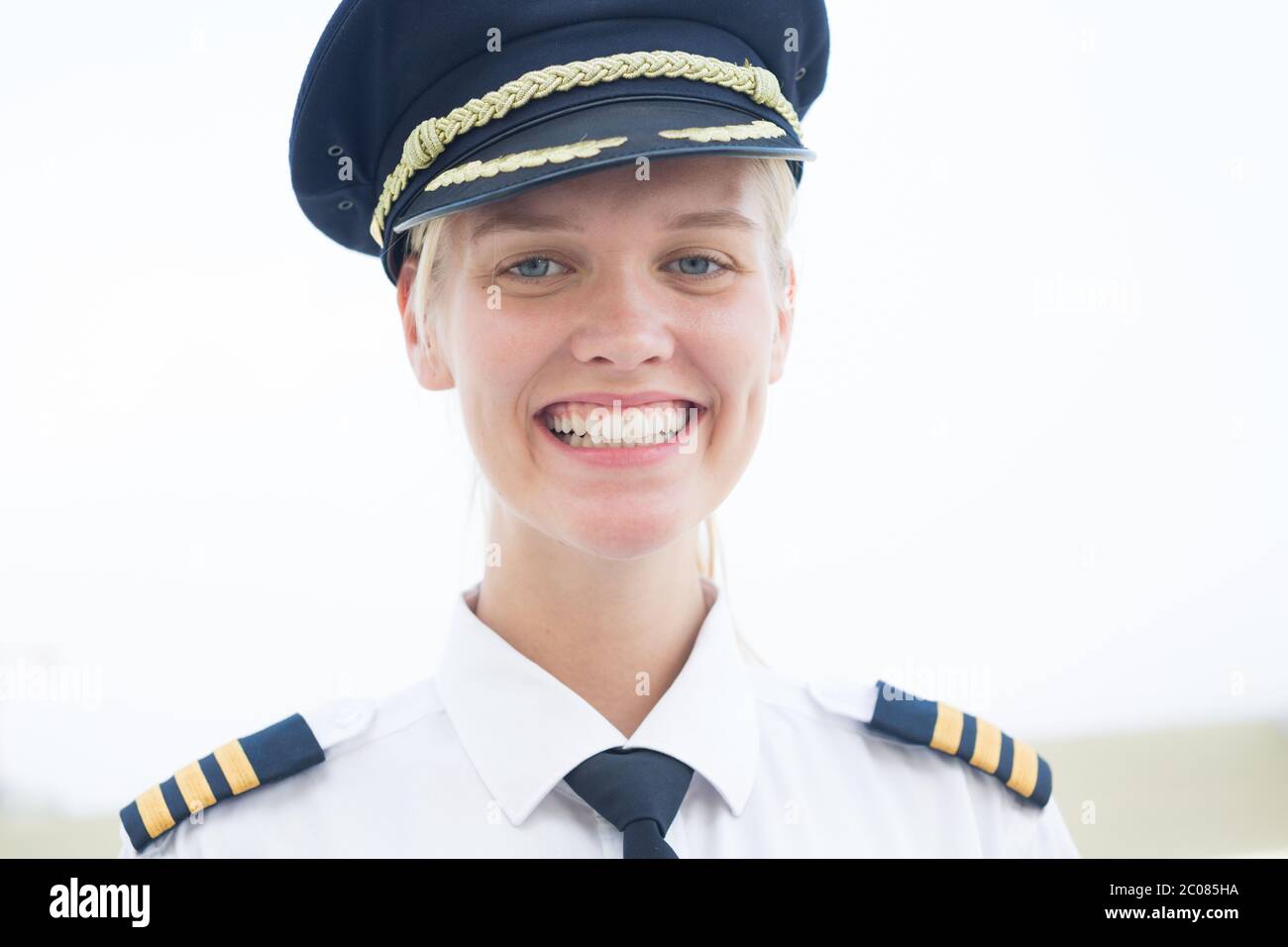 A pretty female pilot smiling into the camera , walking to the plane at