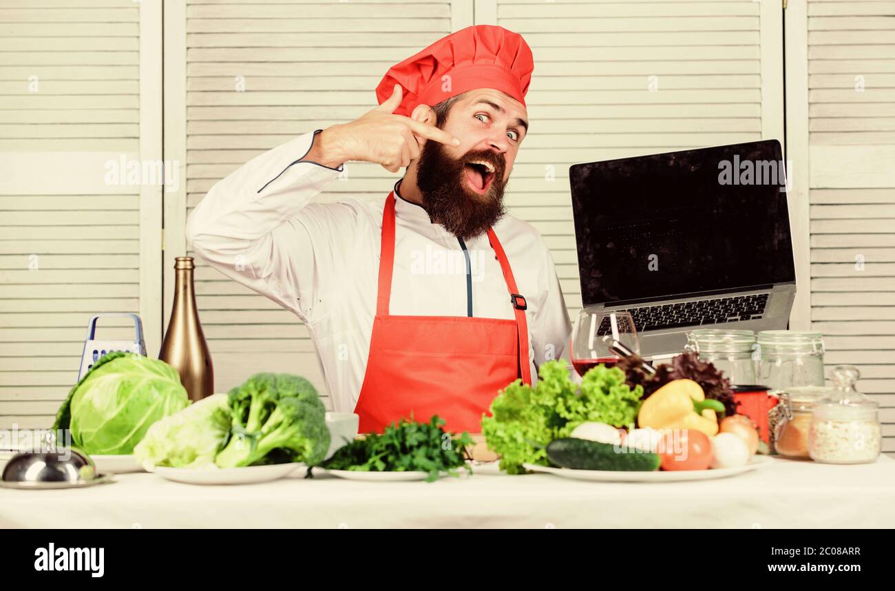 Culinary school. Hipster in hat and apron buy products online. Shopping online. Man chef searching online ingredients cooking food. Grocery shop online. Delivery service. Chef laptop at kitchen. Stock Photo