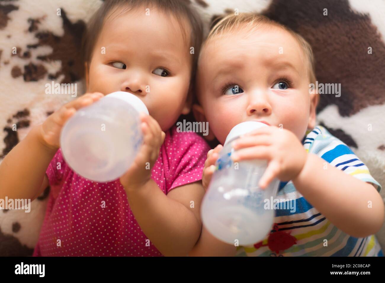 Caucasian white and asian babies lying on the  bed together drinking milk. Stock Photo