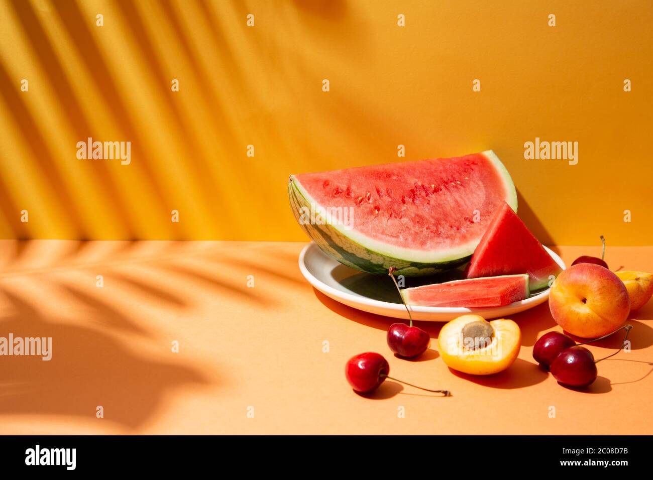 Trendy summer fruit composition with tropical leaves shadows on an orange and yellow set. Copy space Stock Photo