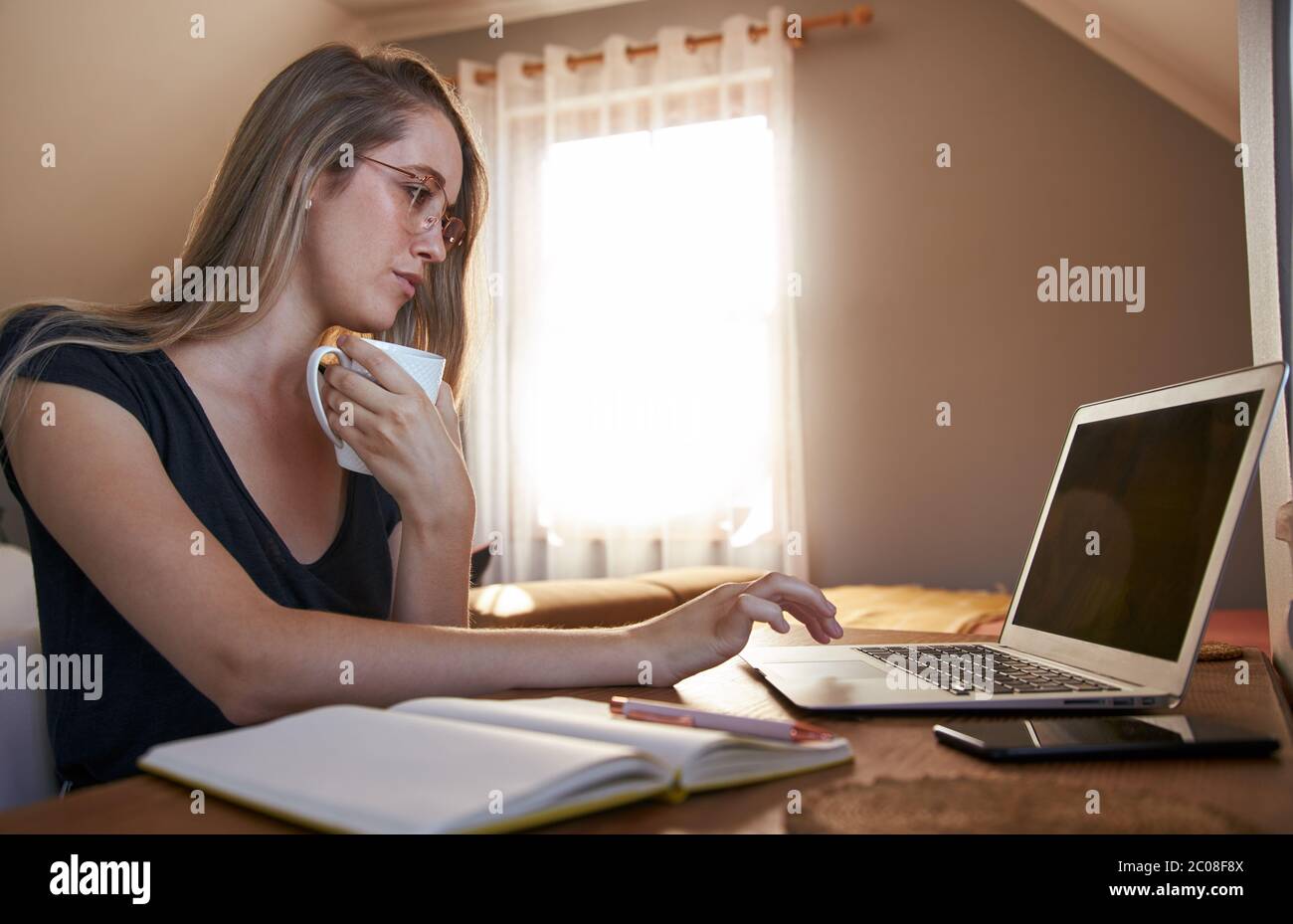 Young female working from home on laptop whilst drinking coffee Stock Photo