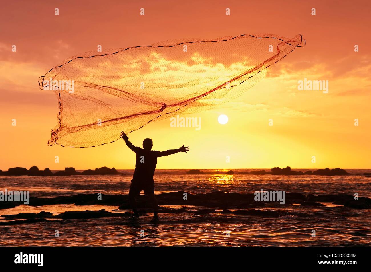 Hawaiian Fisherman (model released) throws a fishing net at sunset in