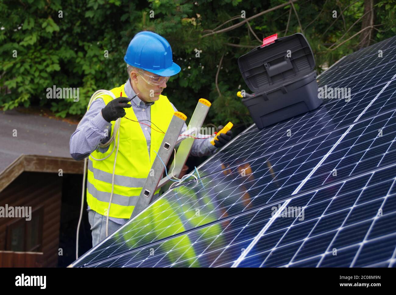 Installation and commissioning of solar panels. Renewable energy in a private home. Worker with electrical appliances on the roof. Stock Photo