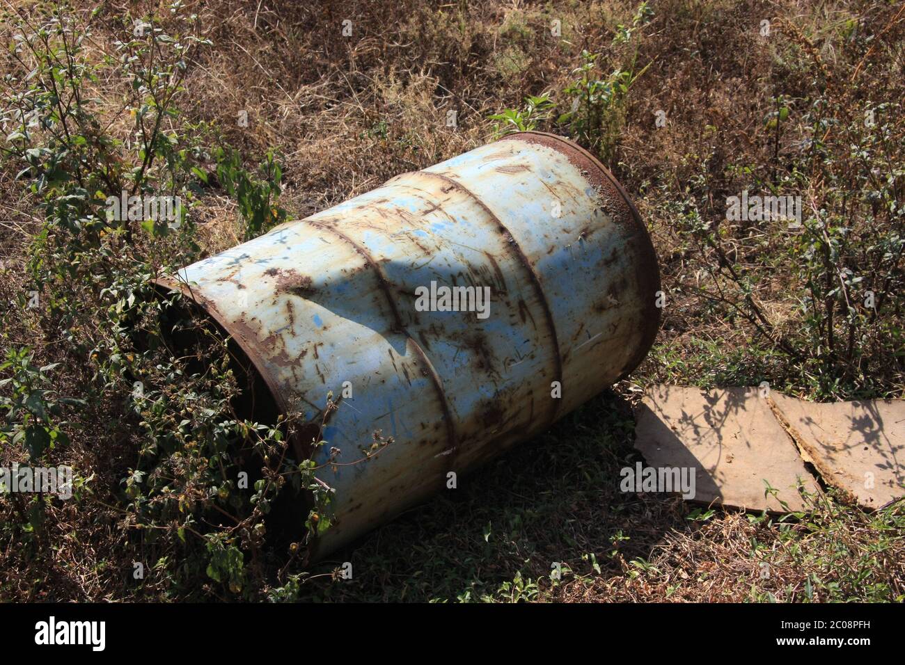 Old Oil Drum/Barrel left damaged on the ground with a dent/dint in the side and surrounded with weeds Stock Photo
