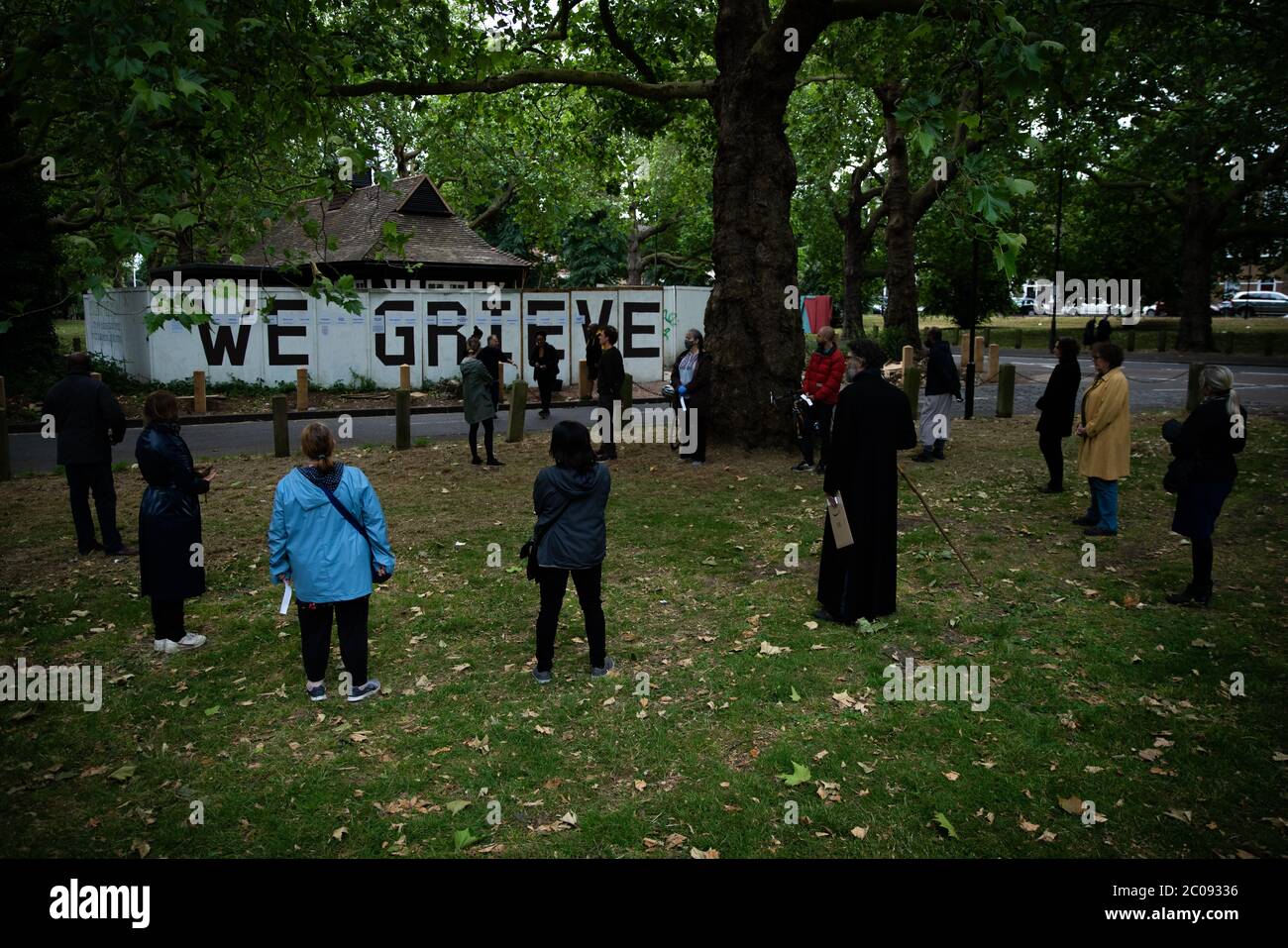 Members of the local community gather at a memorial Wall with the words 'We Grieve' and the names of local people who have died from COVID-19 and other non-coronavirus related causes like terminal illness during the Coronavirus outbreak, written on hoarding around Liberty Hall on Clapton Common, London. Stock Photo