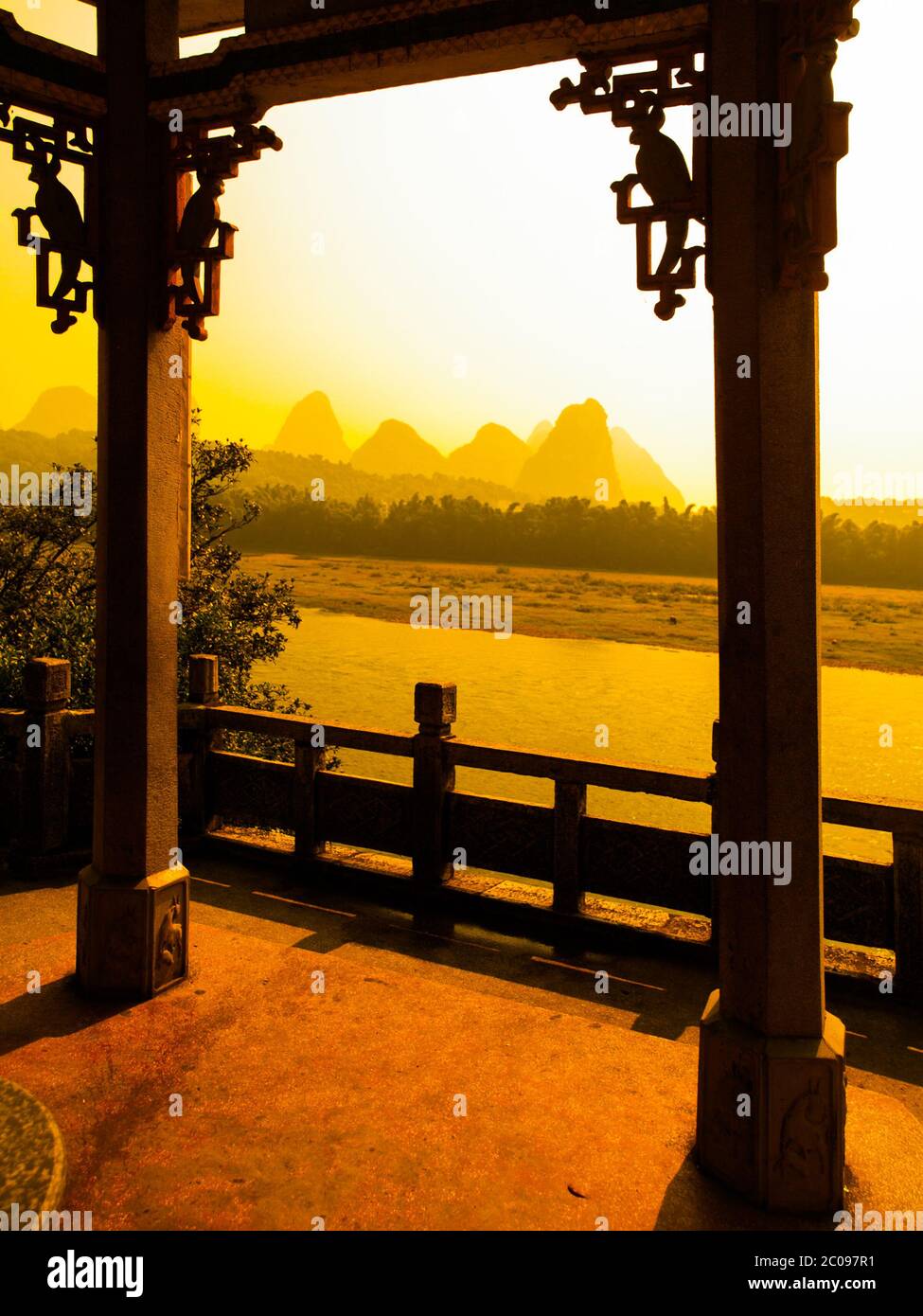 Sunset in karst landscape around Yangshuo an Li River with peaks silhouettes, Guangxi Province, China. View from terrace with ornamental columns. Stock Photo
