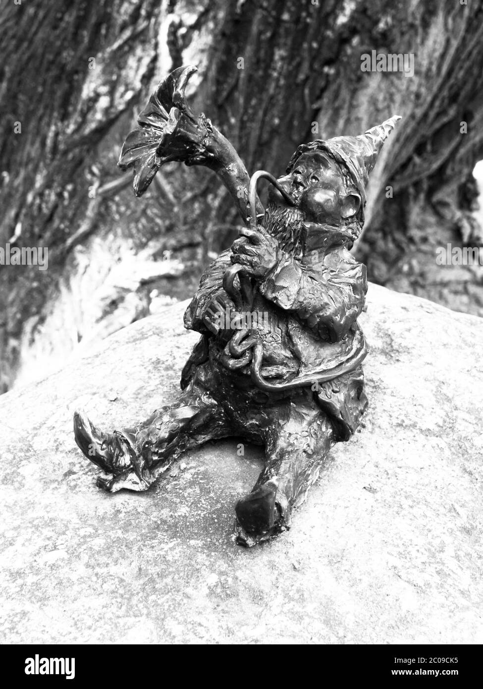 WROCLAW, POLAND - CIRCA 2014: Dwarf playing trombone in Wroclaw botanical garden, Poland, circa 2014. Dwarfs are small figurines hidden on different places in Wroclaw. Black and white image. Stock Photo