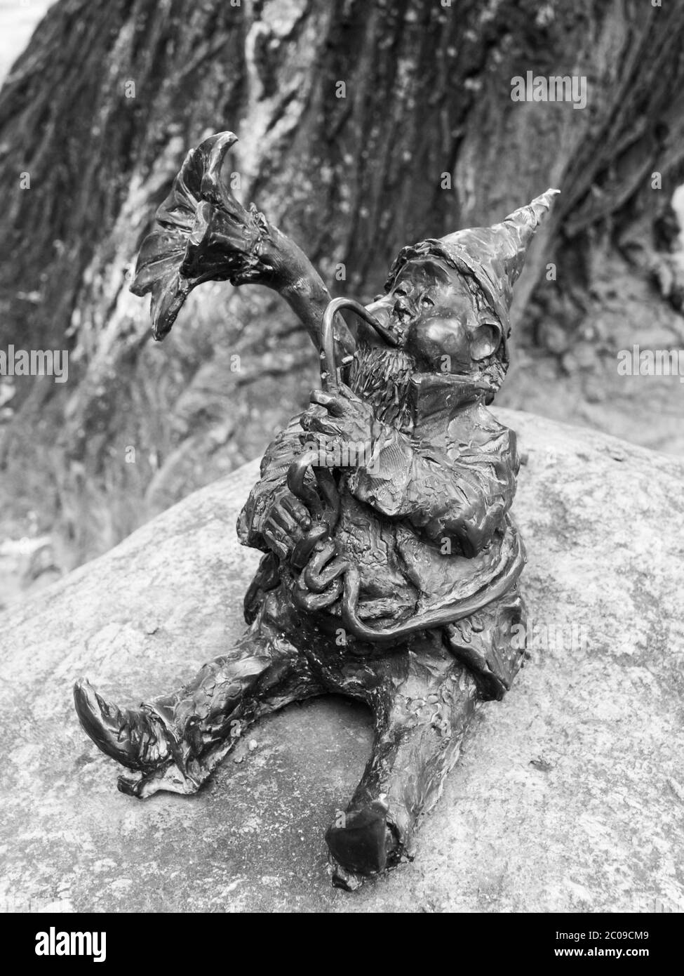 WROCLAW, POLAND - CIRCA 2014: Dwarf playing trombone in Wroclaw botanical garden, Poland, circa 2014. Dwarfs are small figurines hidden on different places in Wroclaw. Black and white image. Stock Photo