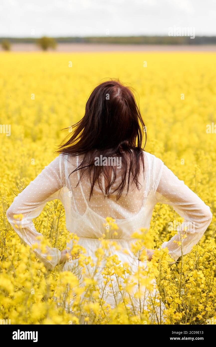 Young woman in a white dress standing in a rapeseed field. Blooming ...