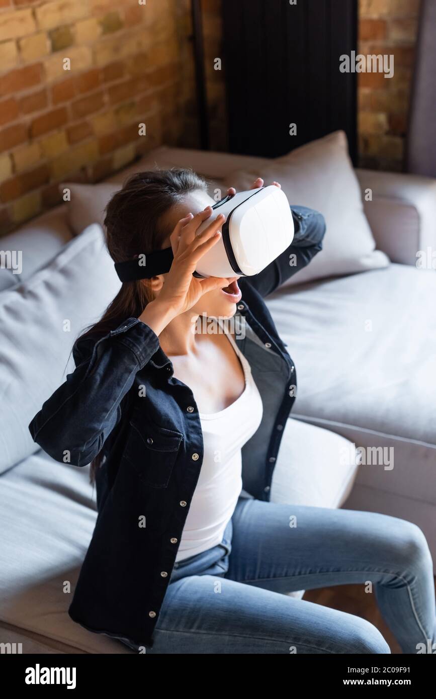 shocked young woman touching virtual reality headset while sitting on ...