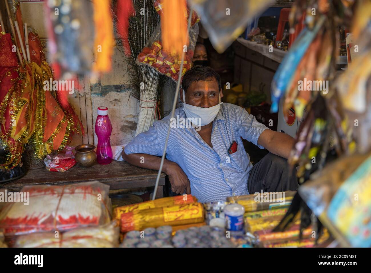 An Indian shopkeeper sells votive threads, coconuts and flower garlands which will be offered by Hindu devotees to the Hindu deities inside  Mandir (T Stock Photo