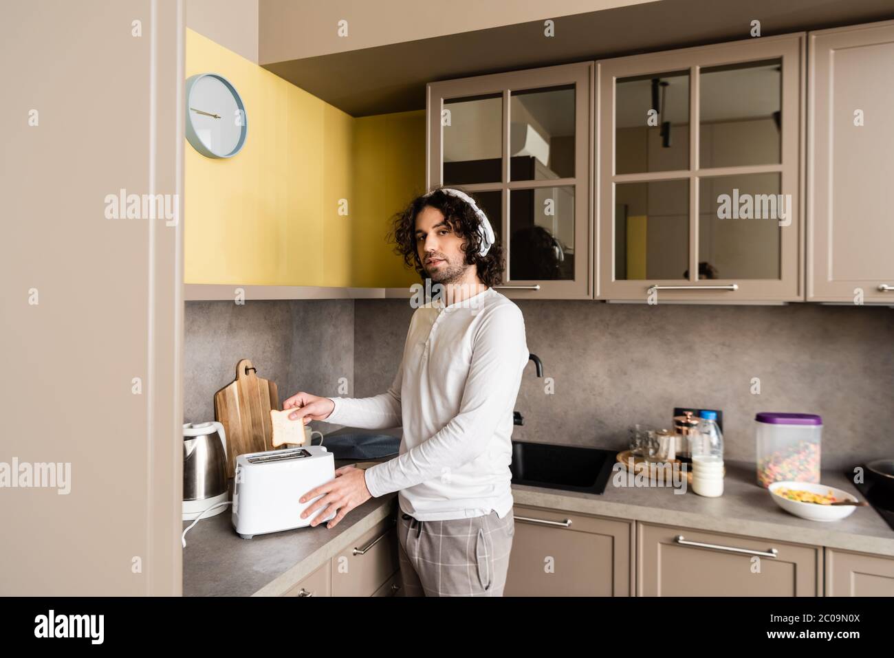curly man in wireless headphones putting bread into toaster while ...