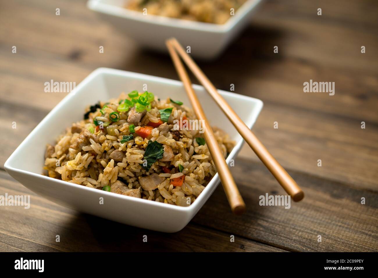 Basil fried rice dish with chopsticks resting on the bowls placed on wooden background. This asian inspired recipe uses lots of fresh ingredients. Stock Photo