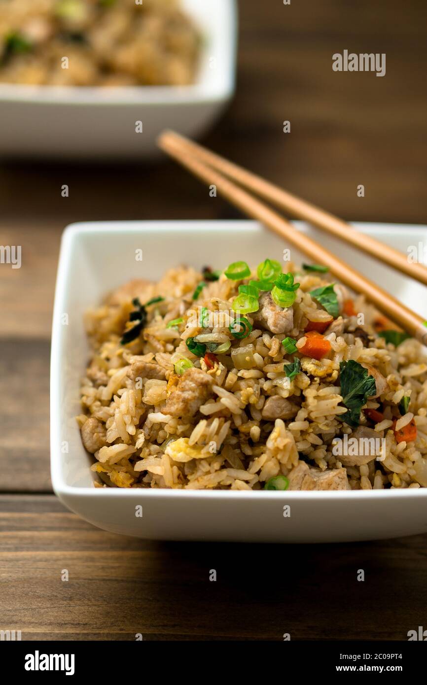Basil chicken fried rice with chopsticks on a wooden background close up view. This thai inspired meal is perfect for a quick lunch or served as side Stock Photo