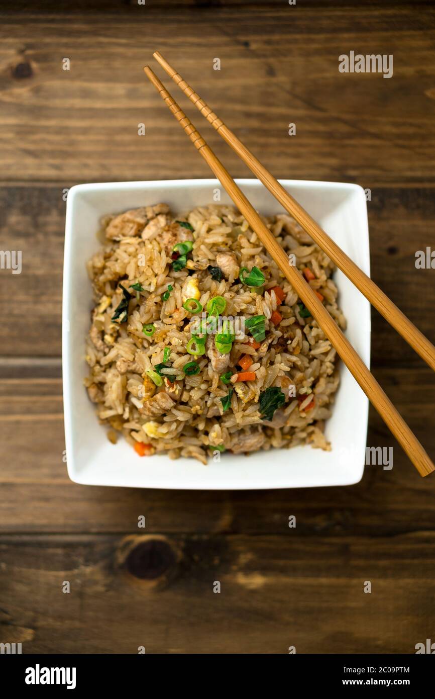 Basil chicken fried rice with chopsticks on a wooden background viewed from above. This thai inspired meal is perfect for a quick lunch or side dish. Stock Photo