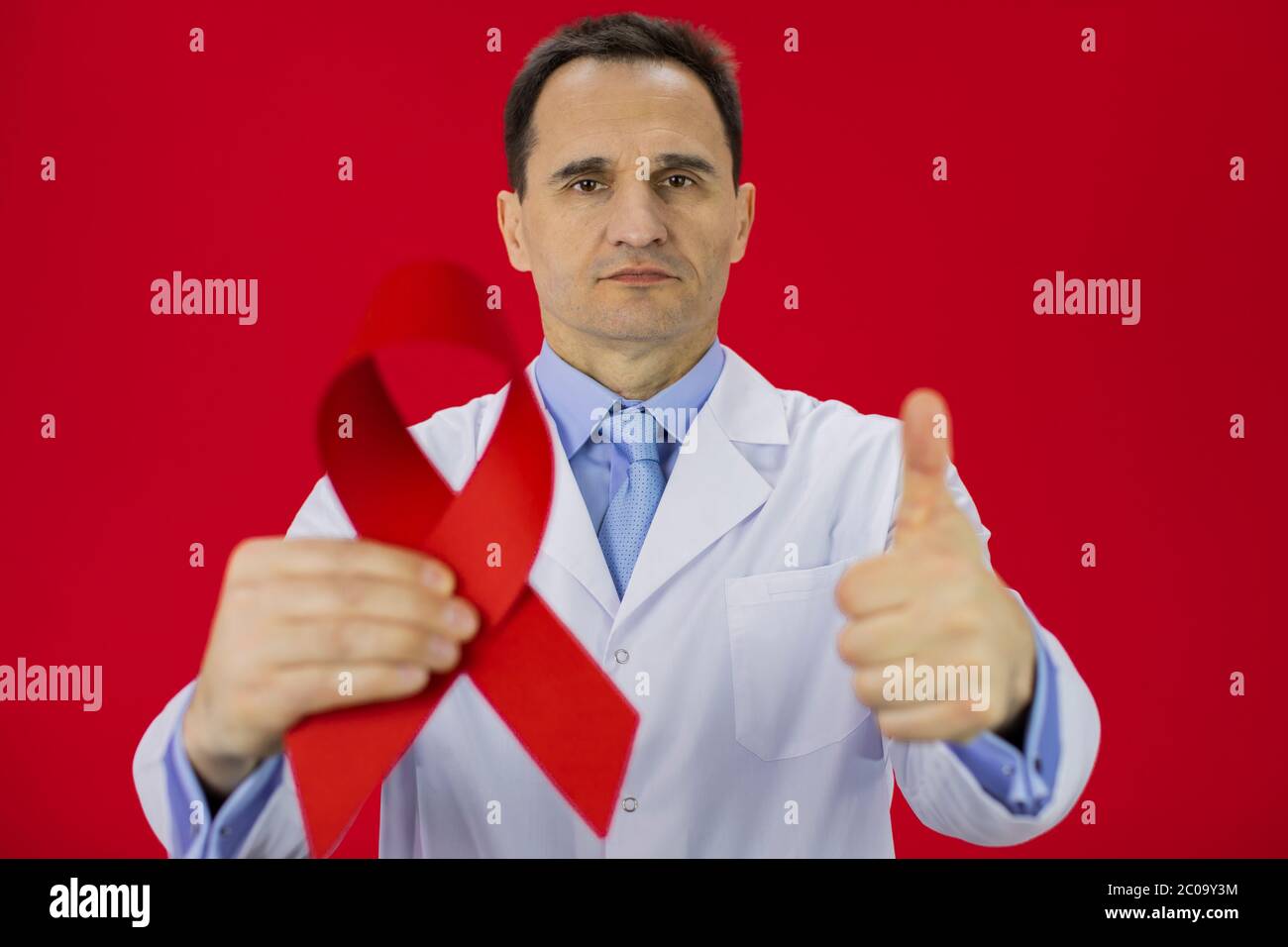 Male doctor in lab coat with red HiV Aids ribbon shows like sign with ...