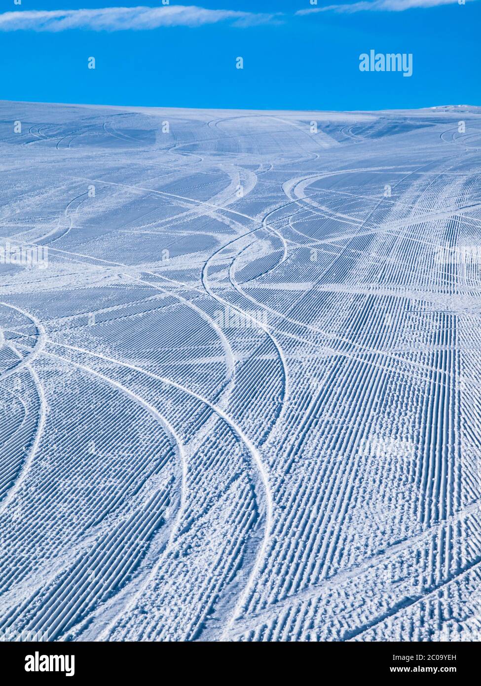 Empty morning ski slope groomed with several tracks from skiers and blue sky Stock Photo