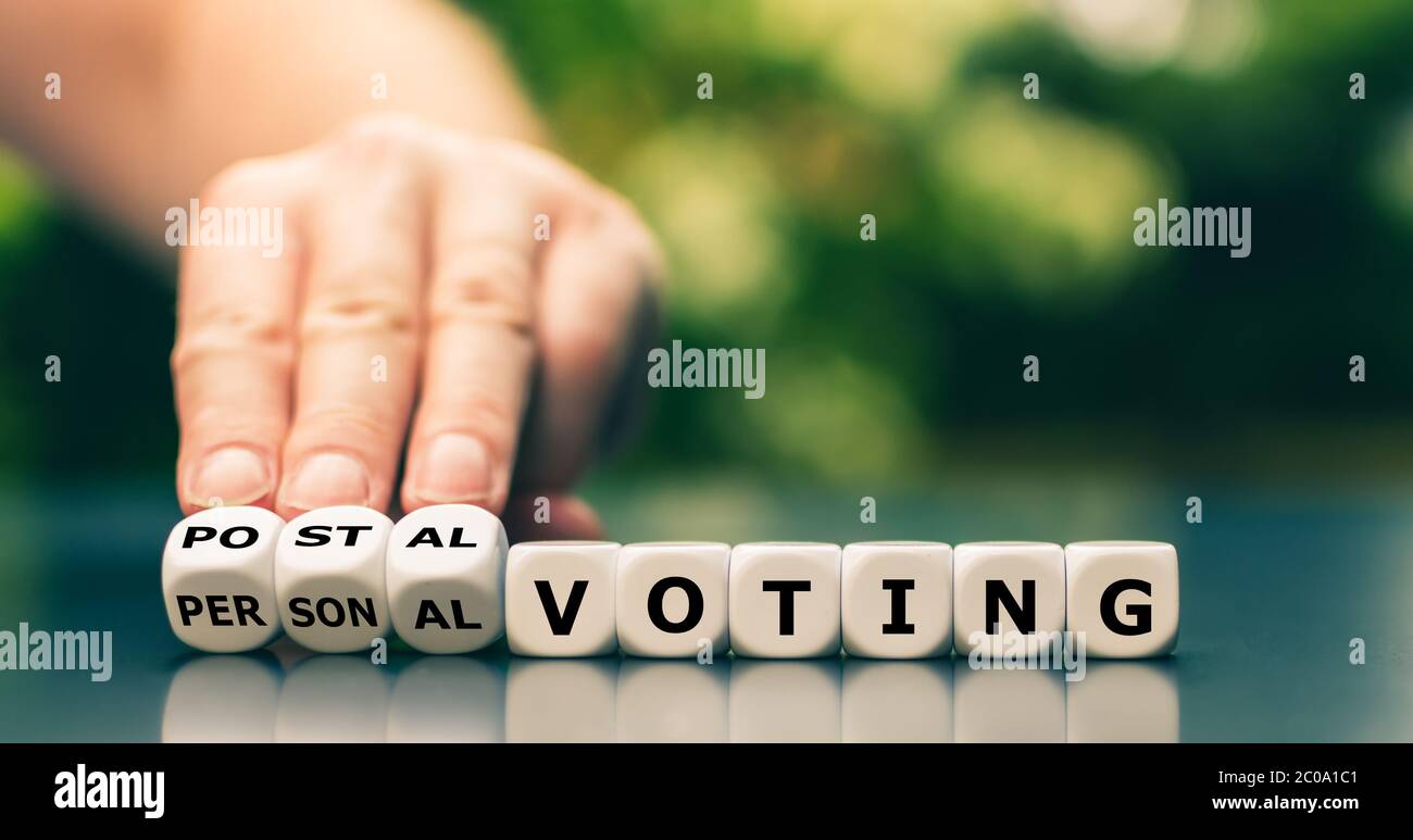 Decision for postal voting. Hand turns dice and changes the expression "personal voting" to "postal voting". Stock Photo