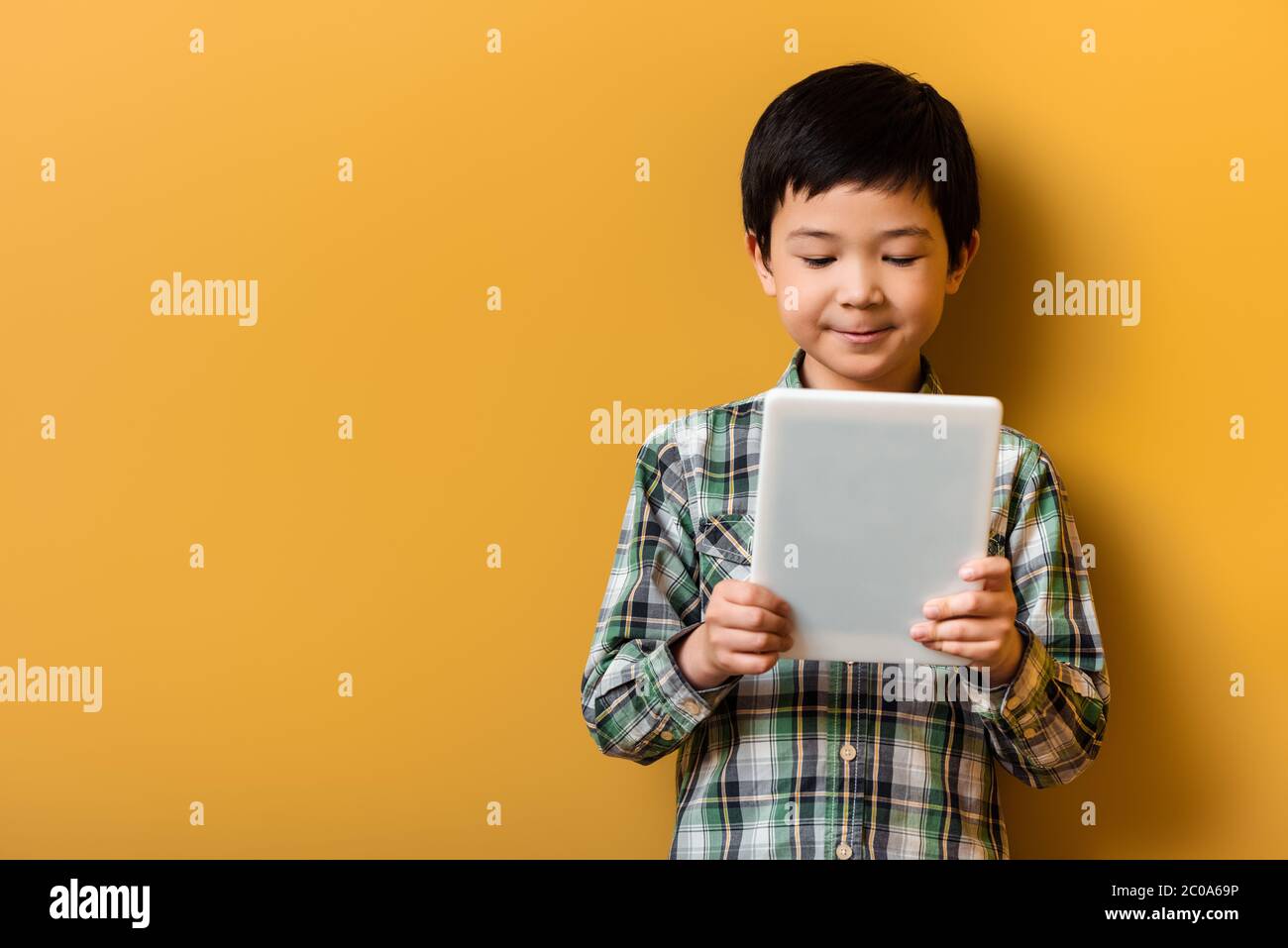 cute smiling asian boy using digital tablet on yellow Stock Photo