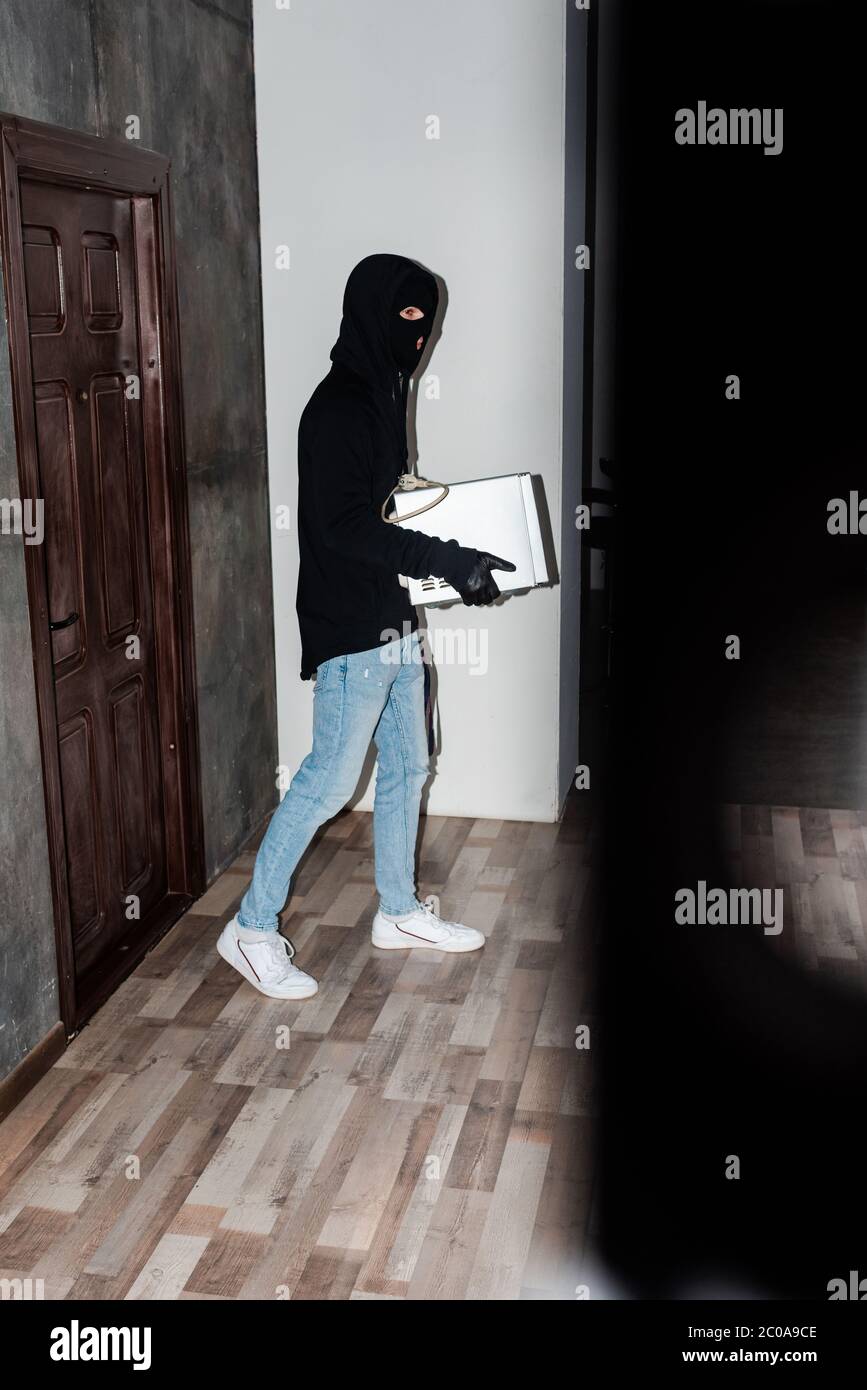 Side view of robber holding microwave oven while walking near house ...