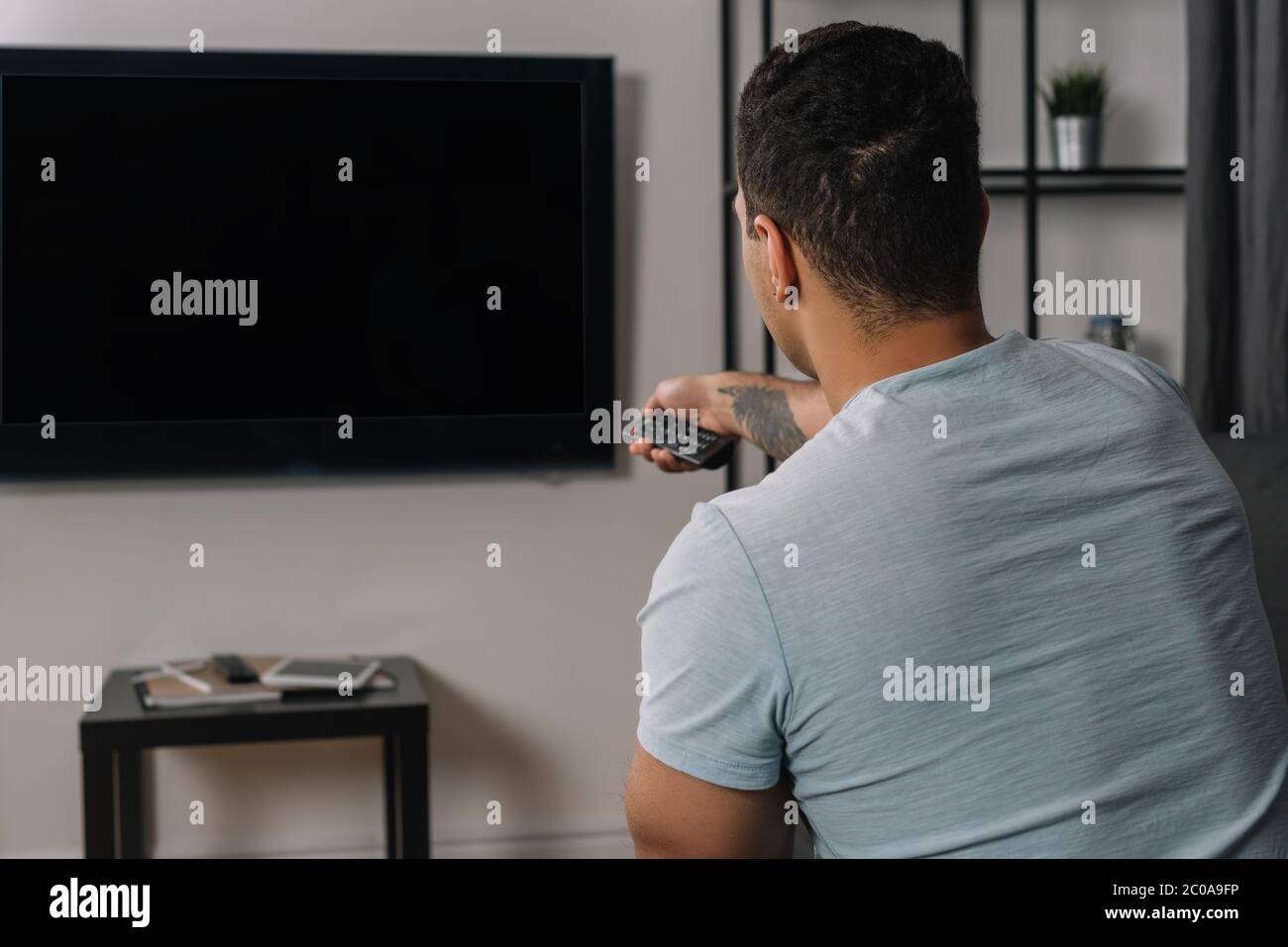back view of mixed race man holding remote controller near flat panel tv with blank screen Stock Photo