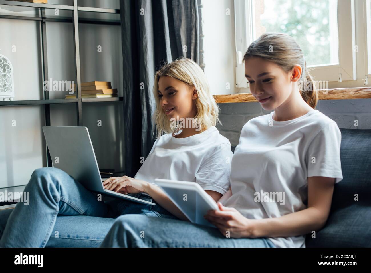 Selective focus of smiling sisters using laptop and digital tablet on ...