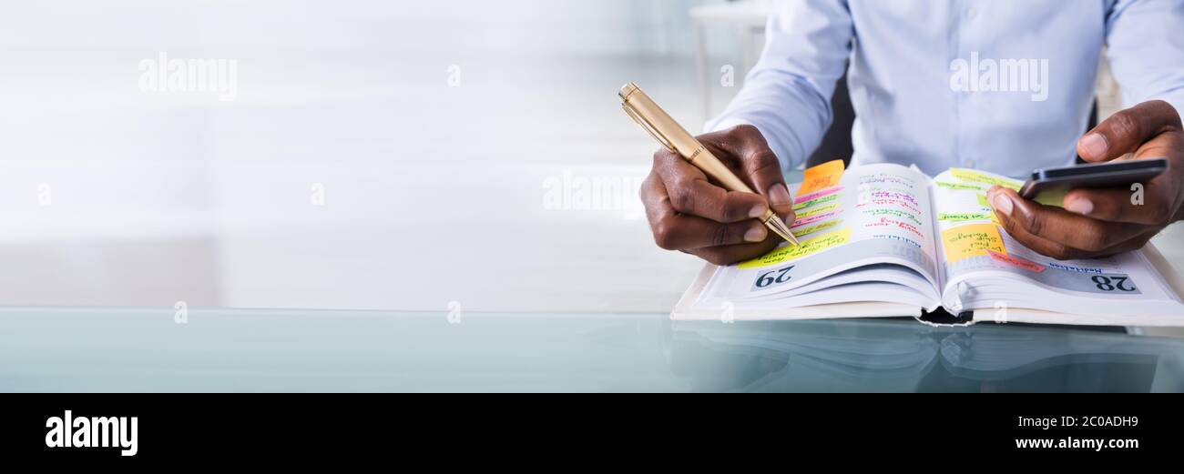 African American Man Writing Tasks And Events In Calendar Book Stock Photo