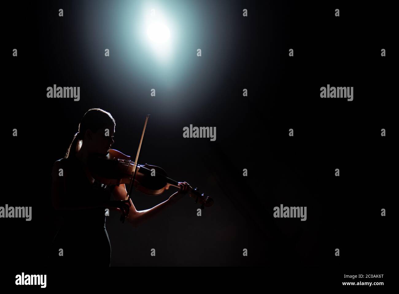 silhouette of female musician playing on violin on dark stage with back ...
