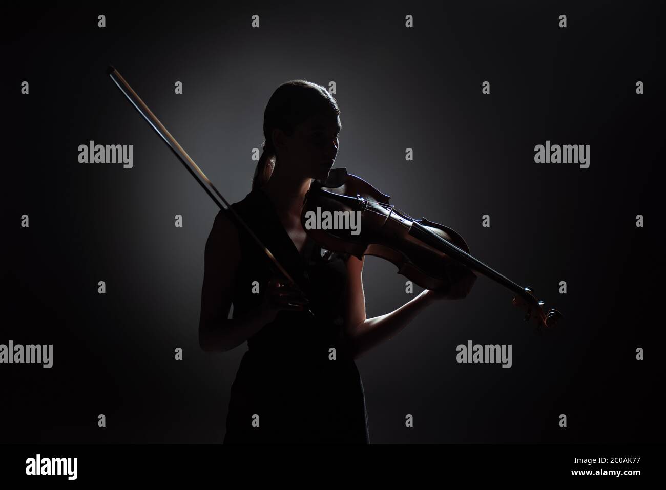 silhouette of professional female musician playing on violin on dark stage Stock Photo