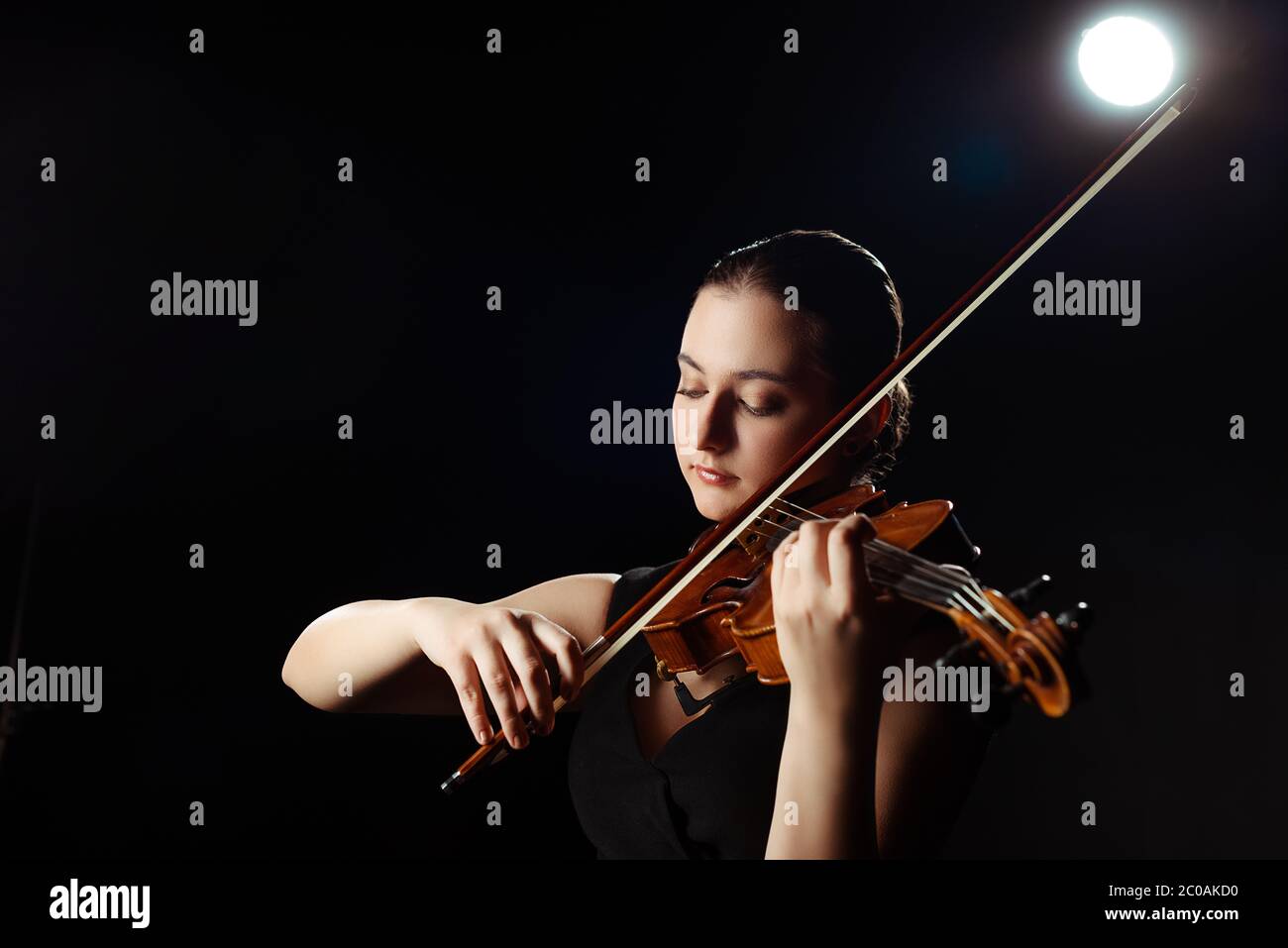 attractive female musician playing on violin on black with back light ...