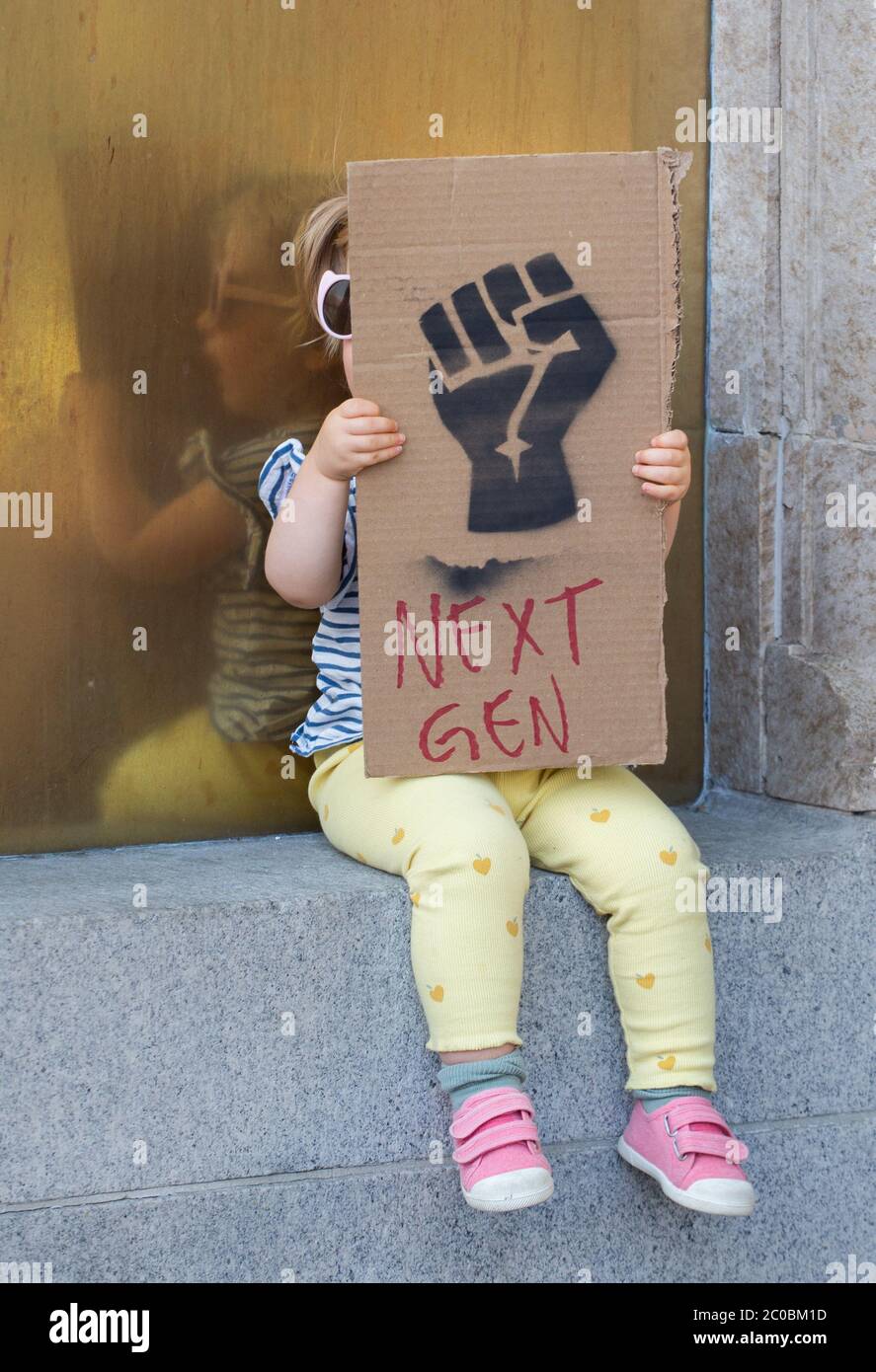 A young white toddler hides behind her sign showing an image of a black fist that symbolizes Black Lives Matter along with the words 'next-gen' during a June 7, 2020 protest in Hollywood California. Stock Photo