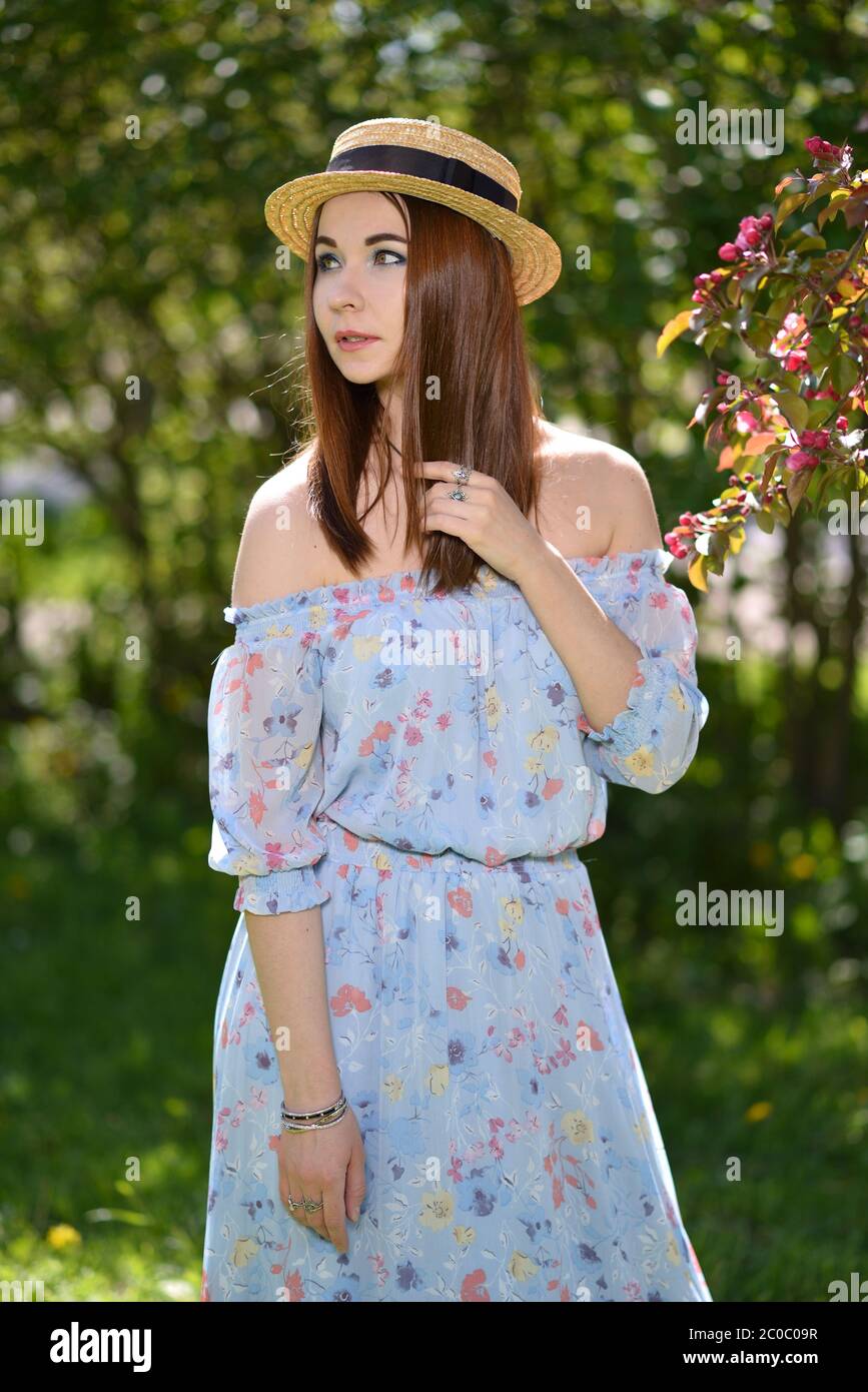 A beautiful girl in a blue dress and a straw hat looks into the ...