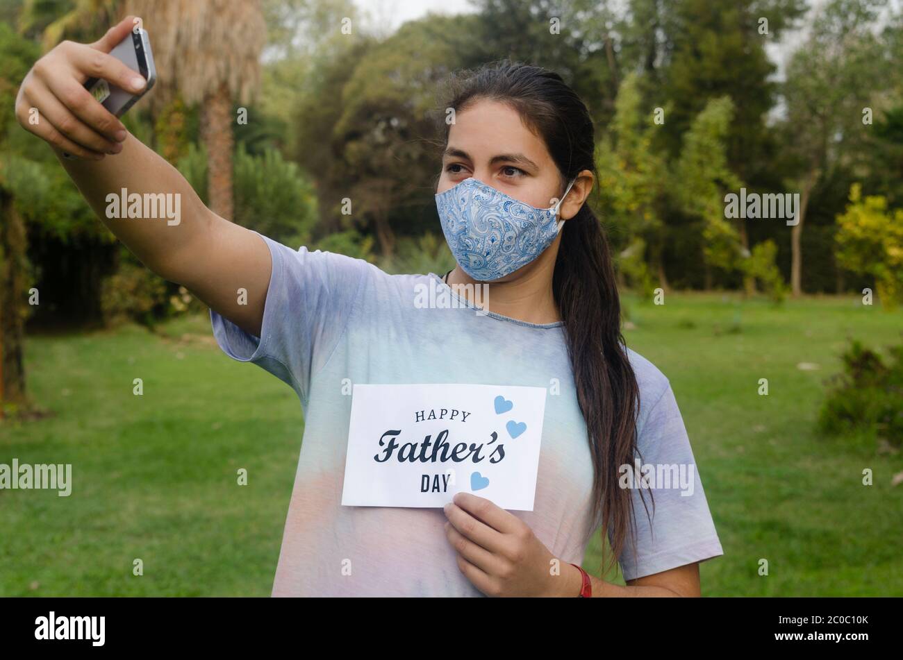 Young girl smiling at cellphone during video call to a father at home for Father's Day. She is holding a white card with the text Happy Father's Day Stock Photo