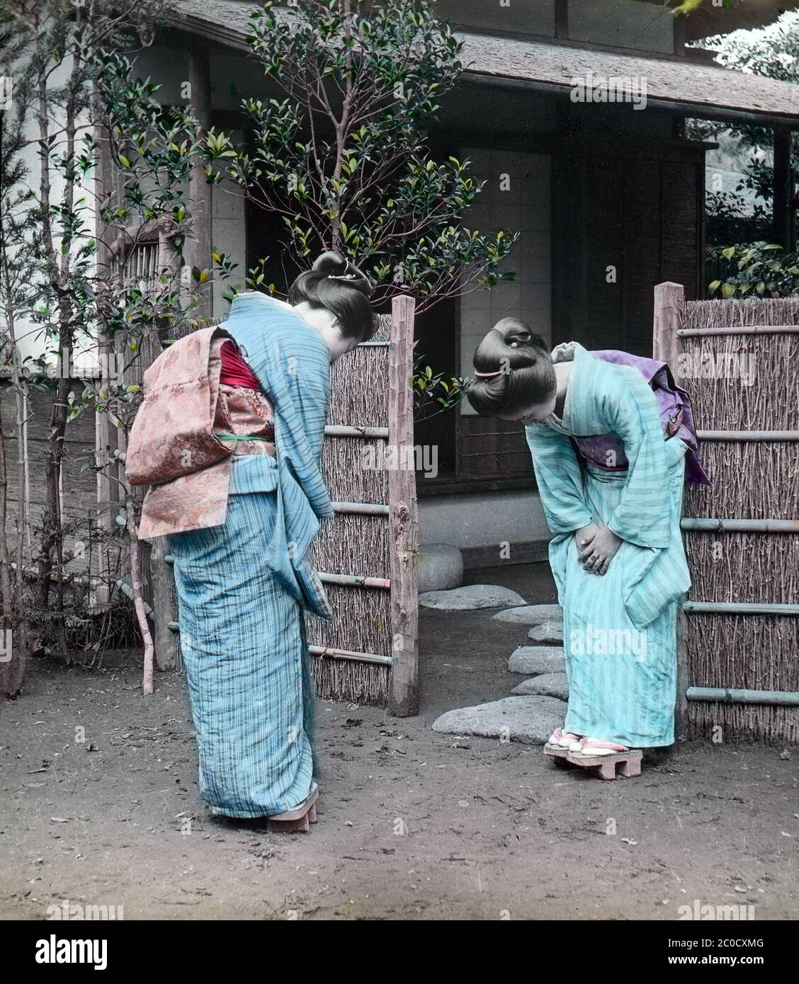 [ 1900s Japan - Women Greeting ] — Two women wearing kimono, geta and traditional hairstyles bow to each other in the yard of a restaurant.  20th century vintage glass slide. Stock Photo