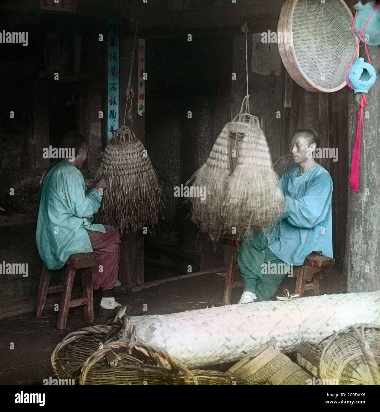 [ 1900s Japan - Chinese Artisans ] — Chinese artisans making straw rain coats in Mukden, Manchuria during the Russo-Japanese War (1904-1905).  The Battle of Mukden (奉天会戦, Hoten kaisen) was fought between Japanese and Russian forces between February 20  and March 10, 1905 (Meiji 38).  It was one of the largest land battles to be fought before World War I and the last and the most decisive major land battle of the Russo-Japanese War. The city is now called Shenyang. It is the capital of Liaoning province, China.  20th century vintage glass slide. Stock Photo