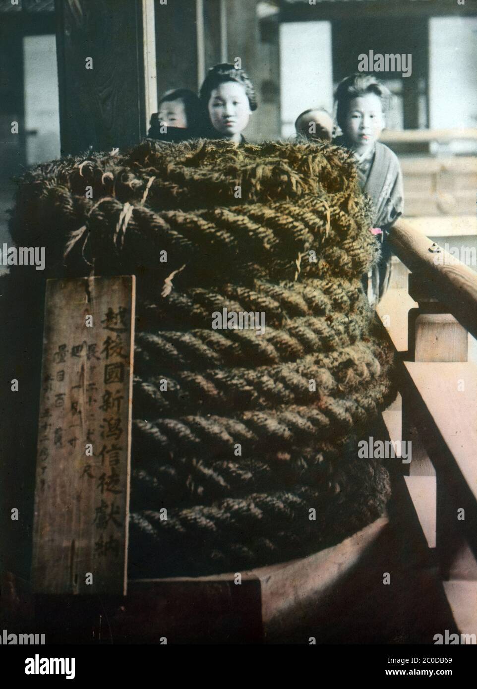 [ 1900s Japan - Rope of Human Hair ] — Two Japanese girls and their charges behind a huge coiled rope, made from human hair, at Higashi Honganji Temple in Kyoto.  During the reconstruction of the temple in 1895 (Meiji 28), there was no rope strong enough to hoist the temple’s massive wooden beams.  In response, female devotees cut off their hair and braided it into strong and thick ropes.  To this day, the rope is still on display, albeit now in a glass case.  20th century vintage glass slide. Stock Photo
