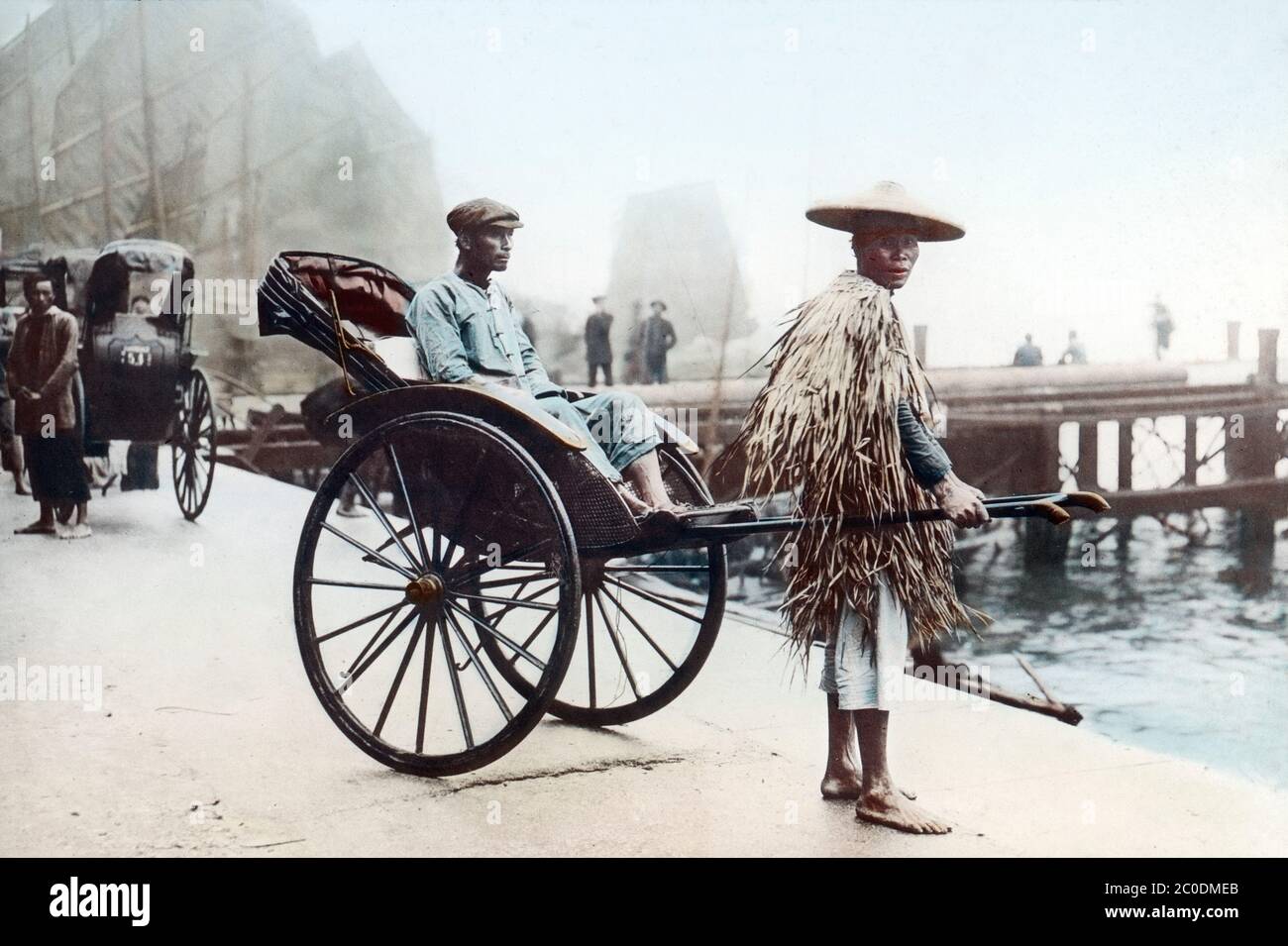 [ 1910s China - Hong Kong Rickshaw ] — A Chinese rickshaw puller wearing a straw raincoat with his customer at Hong Kong Harbor, ca. 1912.  20th century vintage glass slide. Stock Photo