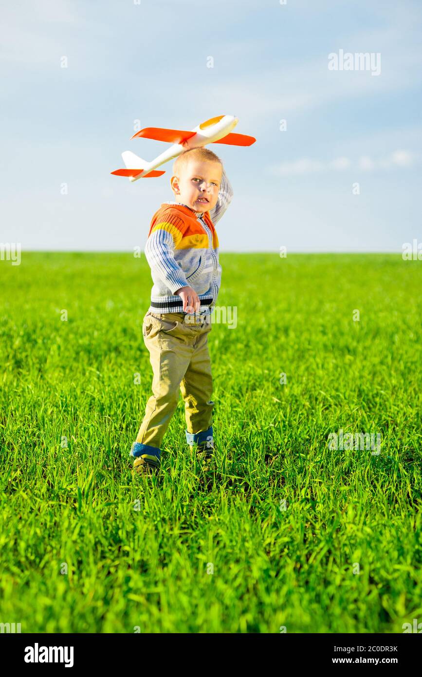 Happy boy playing with toy airplane against blue summer sky and green ...