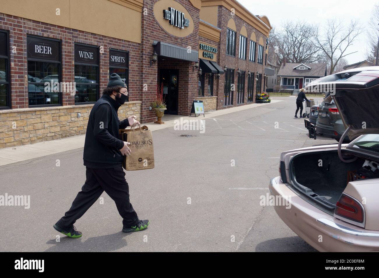 Kowalski's Market man making a delivery to a car trunk of groceries keeping socially distant wearing a mask. St Paul Minnesota MN USA Stock Photo