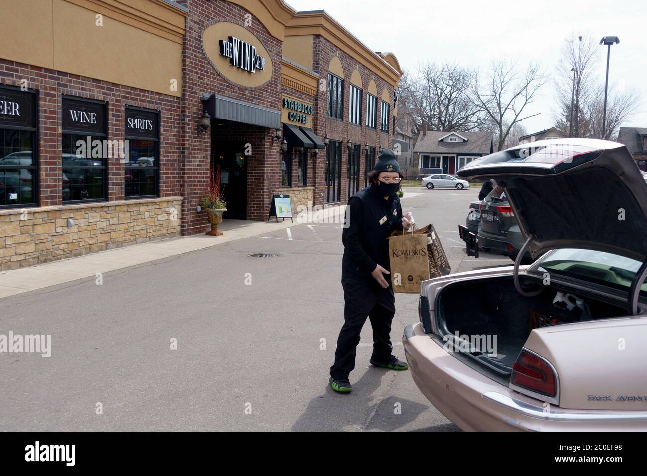 Man delivering ordered groceries to car trunk socially distant wearing a mask. St Paul Minnesota MN USA Stock Photo